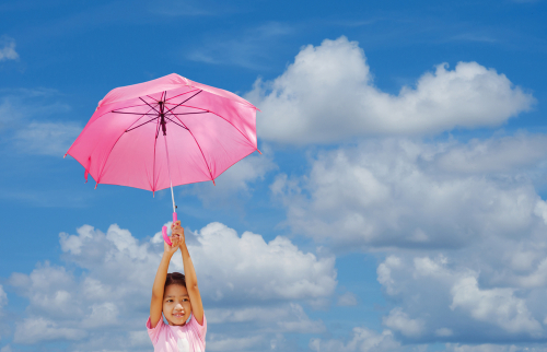 Ein Mädchen hält einen pinken Regenschirm gegen einen klaren, blauen Himmel mit Wolken.