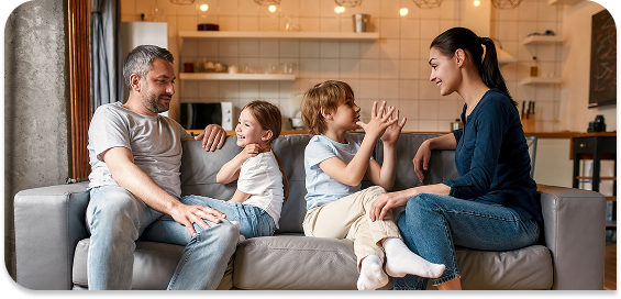 Eine Familie sitzt auf einem Sofa und unterhält sich fröhlich miteinander. Kinder lachen und zeigen Gesten.