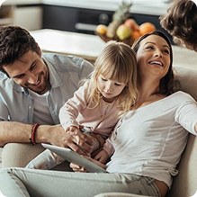 A family sits together on a sofa, enjoying playing with a tablet.
